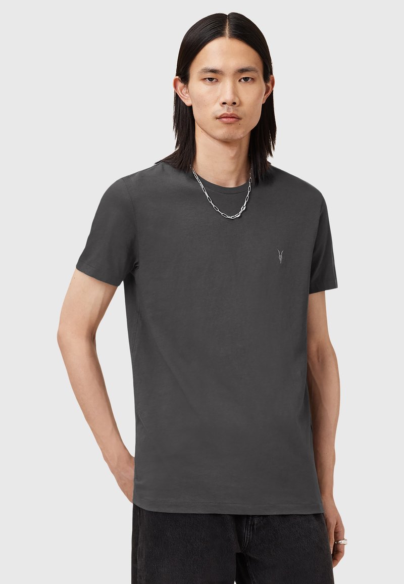 T-shirt grigio a maniche corte realizzato in tessuto morbido, con un piccolo logo sul petto e una vestibilità rilassata, abbinato a jeans scuri.