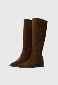 Barna velúr térd fölé érő csizma hegyes orral, oldalsó cipzárral és alacsony, rakott sarkával. Sima textúra és letisztult dizájn.