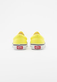 Chaussures à enfiler en toile jaune avec une semelle blanche, des accents noirs et un logo rouge "Vans Off The Wall" sur le talon.