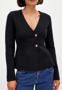 Must have mustad kudum, sügava V-kaelusega, pikkade varrukatega ja kahe esisega nupuga. Pehme tekstuur, keha järgi lõikamine ja peplum hem.