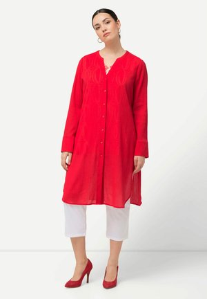 Rode, langärmige jurk met knoopsluiting, gestructureerde stof en een gekartelde halslijn, gecombineerd met witte cropped broek en rode hakken.