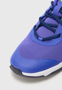 Violette Sportschuhe mit einem Mesh-Obermaterial und einer glatten, synthetischen Zehenkappe, kontrastierenden marineblauen Schnürsenkeln und weißen Akzenten an der Sohle.