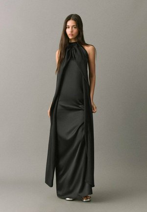 Abito maxi in satin nero con scollo a halter, silhouette fluida e dettagli drappeggiati laterali. Texture liscia con minimi accenti di hardware.