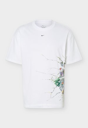 T-shirt blanc Nike avec petit logo noir près du col et motif floral coloré avec des branches sur le côté droit.