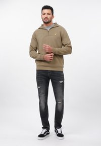 Oliwkowy hoodie z półzamkiem, szary t-shirt pod spodem, do tego podarte czarne dżinsy i czarne buty Vans.