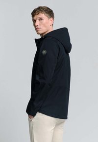 Zwarte waterdichte jas met capuchon, gemaakt van een gestructureerde stof, met zijzakken en een kenmerkend hexagonaal patch op de linkerschouder.