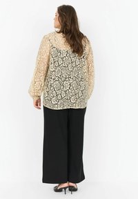 Beige ja must pitsblus, millel on lillemustrid, pikad puffvarrukad ja voolav disain. Kombineeritud avarate mustade pükstega.