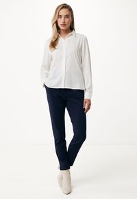 Camicia bianca a maniche lunghe con colletto, abbinata a pantaloni slim fit blu navy, completata da stivaletti beige alla caviglia. Design semplice e pulito.