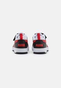 Baskets de sport noires et rouges avec des accents blancs, présentant une texture en cuir lisse et un logo rouge bien en vue à l'arrière du talon.