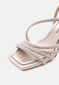 Ασημί σανδάλι ανοιχτού δακτύλου με τετράγωνη μύτη, διακοσμημένο με λεπτά λουράκια που φέρουν μικρές λαμπερές πέτρες.