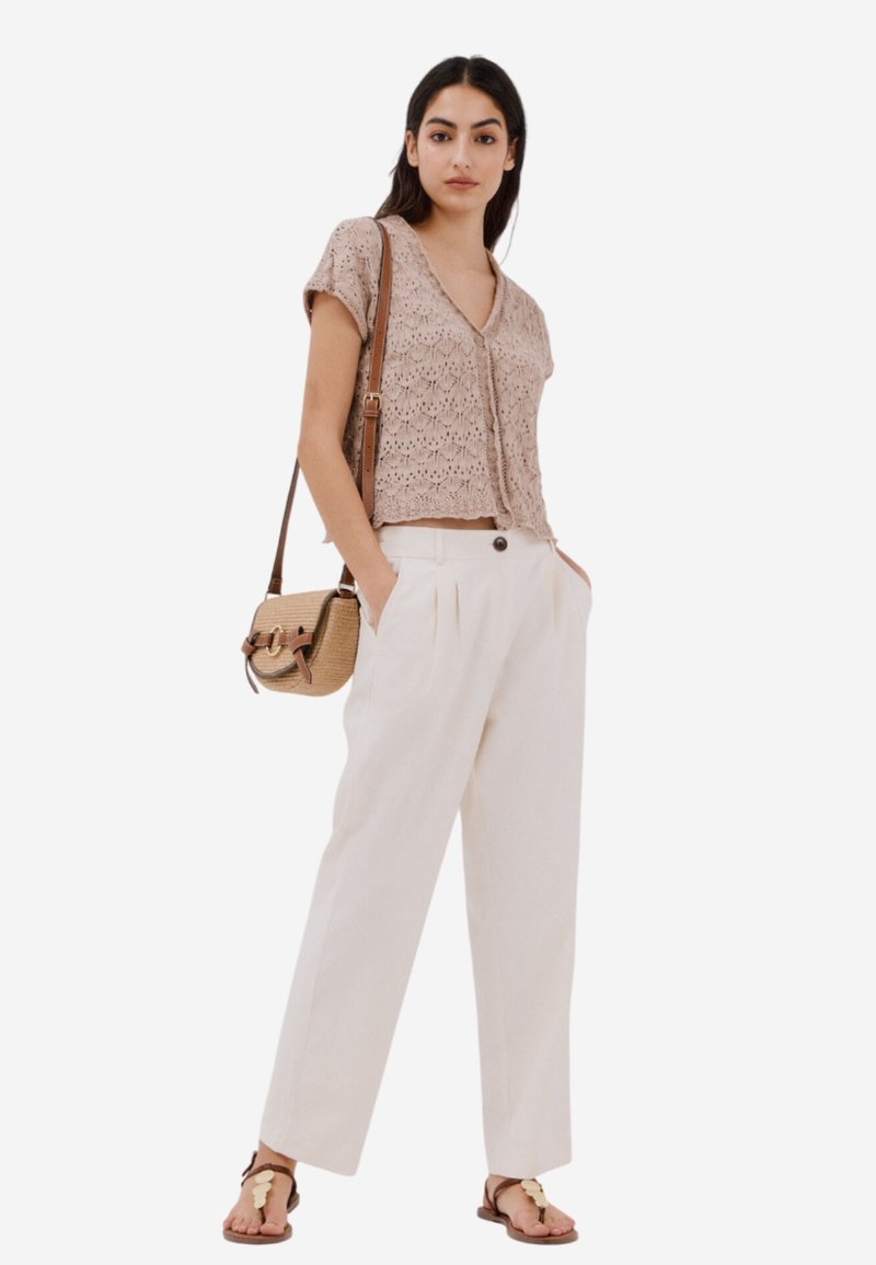 Krämsfärgade linnebyxor i kombination med en ljusbeige stickad topp. Utfitten inkluderar en liten vävd väska och platta sandaler med bladdekorationer.