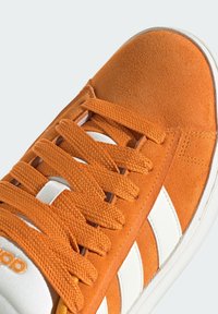 Zapatilla de ante naranja con rayas blancas, cordones gruesos naranjas y una suela blanca, mostrada en primer plano desde arriba.