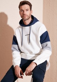 Hoodie s dizajnom u blokovima boja u bijeloj, mornarsko plavoj i sivoj. Ispisani tekst "želim živjeti" na prsima. Mekana, teksturirana tkanina.