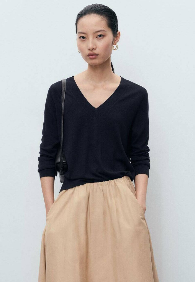 Mørkeblå V-hals sweater med lange ærmer, parret med en beige, let skørt med taljesamling. Enkel design, blød tekstur og minimale detaljer.
