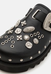 Sabots en cuir noir ornés de clous décoratifs en argent et d'embellissements. Ils présentent une semelle plate-forme épaisse et un accent de boucle pour la fermeture.