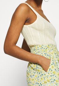 Světlý žlutý žebrovaný top bez rukávů se širokým ramínkem, spárovaný s květinovými šortkami v žluté a zelené barvě, které mají elastický pas a boční kapsy.