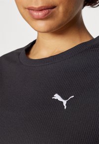 Camiseta de manga corta gris oscuro de canalé con cuello redondo, que presenta un logo de Puma bordado en blanco en el área del pecho izquierdo.