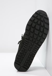 Baskets noires avec un dessus en mesh texturé et une semelle en caoutchouc à motifs avec des rainures profondes pour une meilleure traction. Détails matériels minimalistes.