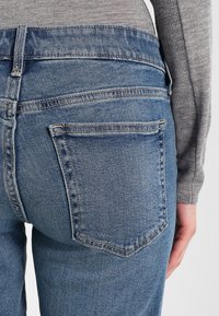 Jeans in denim blu con una forma aderente, dotati di tasche posteriori, cuciture sottili e una texture leggermente sbiadita.