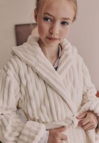 Peignoir en fausse fourrure crème, avec texture côtelée verticale, large col et ceinture nouée. Matière douce et moelleuse avec manches longues.