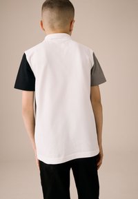 Fehér testű, fekete és szürke ujjú galléros pólóing. Puha anyagból készült, alkalmas hétköznapi viseletre.