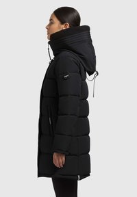 Melnas pūkainas jaka ar augstu apkakli, rāvējslēdzēja aizdari un regulējamu kapuci. Satur ieliktus šuves un diskrētas sānu kabatas.