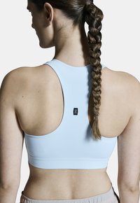 Hellblauer sportlicher Sport-BH mit Racerback-Design, glatter Textur und kleinem schwarzem Logoetikett auf der Rückseite.