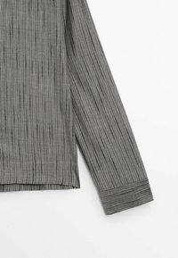 Camicetta a maniche lunghe grigia a righe con linee metalliche sottili, caratterizzata da un orlo dritto e un polsino con bottone, realizzata in un tessuto morbido e textured.