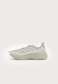 Light gray athletic shoe with white accents, featuring a thick sole and textured upper, and an orange lace detail.
