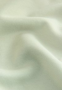 Close-up af lysegrønt strikket stof med en blød, tekstureret overflade og blide folder, der skaber subtile skygger.