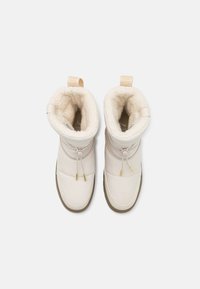 Botas aislantes de color beige claro con un suave forro interior crema, bordes redondeados, cierre ajustable con toggle y suela de caucho.