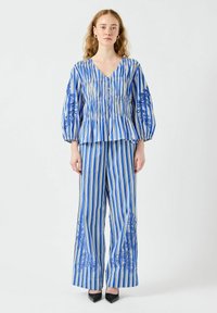 Blå och vit randig tvådelad outfit som består av en v-ringad peplumtopp med puffärmar och vida byxor, prydd med blommig broderi.