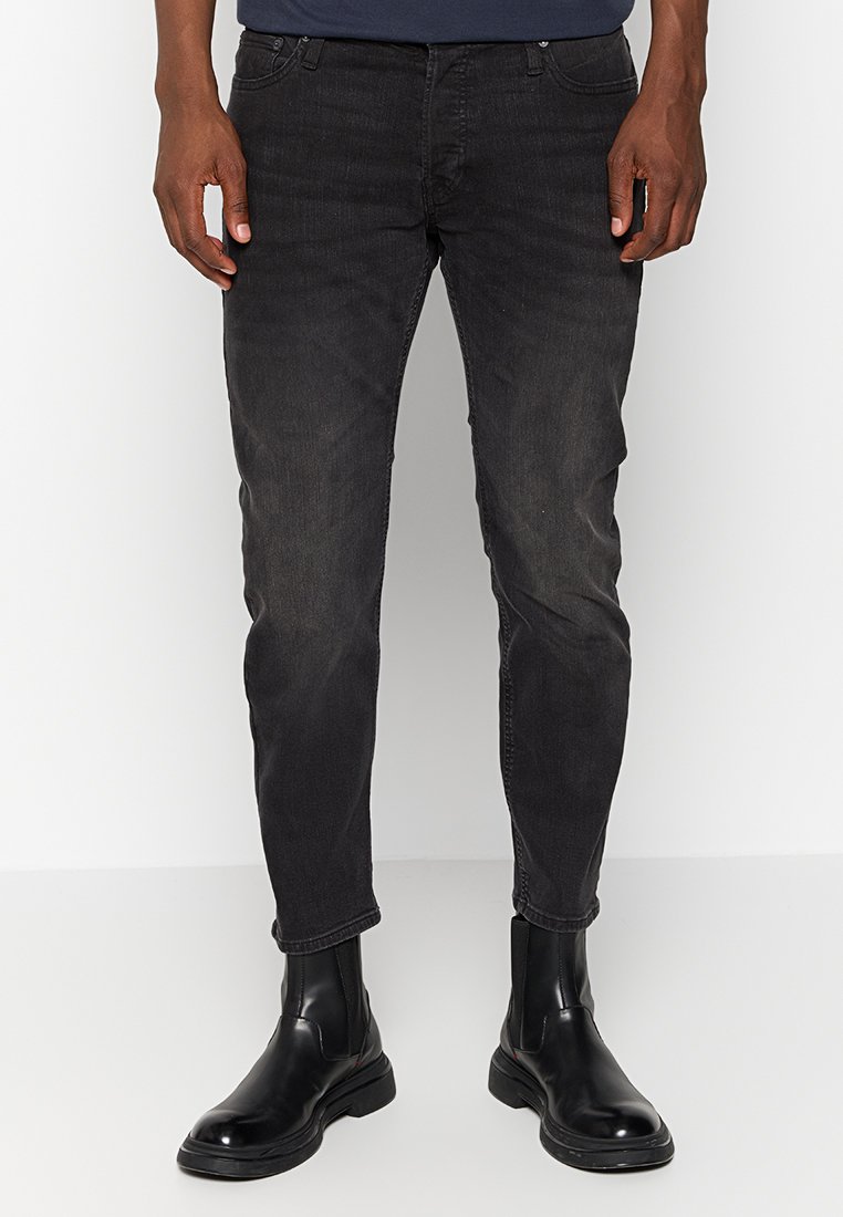 Schwarze Denim-Jeans im Slim-Fit, Fünf-Taschen-Stil, mit subtilen Verwaschungen und leicht tailliertem Bein. Getragen mit schwarzen Stiefeletten.