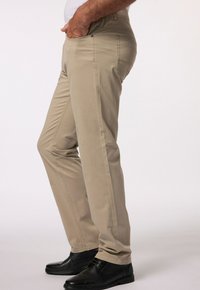 Beżowe spodnie o prostym kroju, z bocznymi kieszeniami i widocznymi szwami, w połączeniu z czarnymi butami. Materiał wydaje się gładki i lekki.