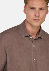 Camicia button-up in lino marrone con tessuto texurizzato, dotata di colletto classico e bottoni visibili lungo la parte anteriore.
