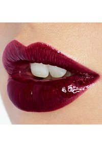 Glossy dark red lips slightly parted, revealing two upper front teeth against light skin background.
