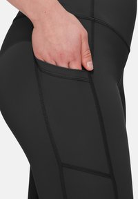 Leggings noirs avec une poche latérale, des coutures texturées et un tissu lisse et extensible, conçues pour le confort et la fonctionnalité.