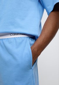 Σετ από γαλάζιο βαμβακερό μπλουζάκι και σορτς με λευκή μέση που φέρει μαύρο λογότυπο "Calvin Klein". Casual εφαρμογή με λεπτομέρεια πλαϊνής τσέπης.