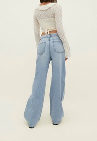 Jeans de mezclilla de corte ancho en azul claro con una cintura alta, con bolsillos traseros y detalles de costura, acompañados de una blusa de encaje blanco texturizado.