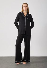 Set di pigiama nero composto da maglia a maniche lunghe con piping bianco e pantaloni coordinati. Tessuto morbido, vestibilità comoda e design a gamba larga.