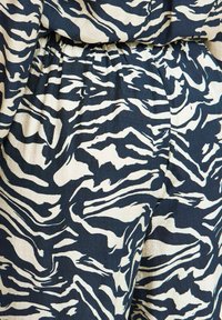 Tkani s uzorkom zebra u tamnoplavoj i boji slonovače, s teksturiranom površinom i naboranim pojasom.
