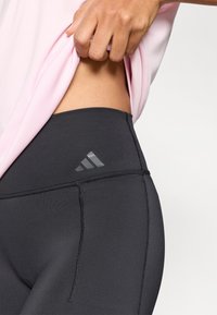 Zwarte sportlegging met een hoge tailleband, voorzien van een reflecterend grijs logo, gestikte details en een gladde, rekbare stof.