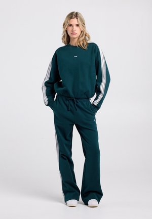Ensemble sweat-shirt et pantalon couleur sarcelle avec bandes blanches sur les côtés. Tissu doux et sportif ; coupe décontractée ; taille ajustable ; col rond.