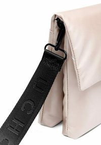 Béžová nylonová taška se strukturovaným designem, vybavená černým texturovaným popruhem a elegantním uzavíracím mechanismem.