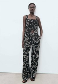 Svart mönstrad bustier-topp och matchande vida byxor med vita abstrakta mönster, med en slät textur och minimala metallaccenter.