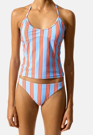 Kobieta nosząca niebiesko-czerwony tankini w pionowe paski z ramiączkami typu halter.