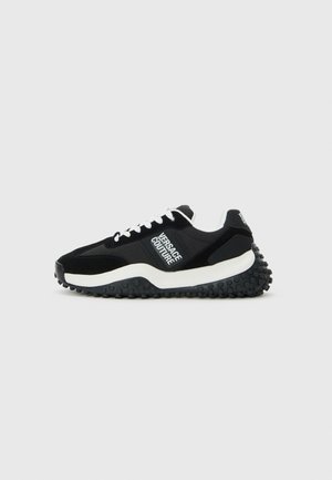 Schwarzer Sportschuh mit weißen Akzenten, aus Wildleder und Mesh-Materialien, auffälliges Logodesign, dicke strukturierte Sohle mit Gummihöckern.