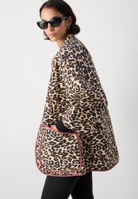 Leopardenmuster Übergröße Jacke mit pinkem Besatz, ausgestattet mit einer großen Tasche und strukturiertem Stoff, kombiniert mit dunklen Hosen und Sonnenbrille.
