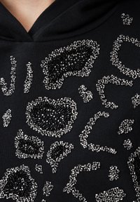 Felpa nera con decorazioni in perline nere e argentate a texture in un design astratto a maculato. Tessuto liscio con scollatura ampia.