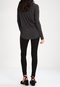 Top nero a maniche lunghe con orlo arrotondato, abbinato a pantaloni skinny neri. Sandali con tacco e cinturini alla caviglia. Tessuto strutturato, design aderente.